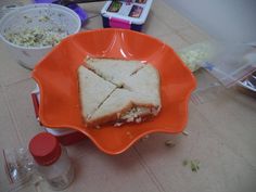 an orange plate topped with a cut in half sandwich on top of a table next to bowls of food