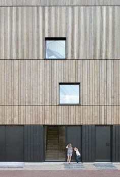 two people standing in front of a building with windows on each side and stairs to the second floor