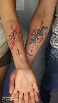 two people are holding hands with tattoos on their arms and both have compasss on them