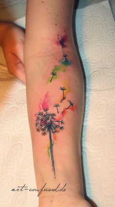 a woman's arm with a watercolor dandelion tattoo design on it