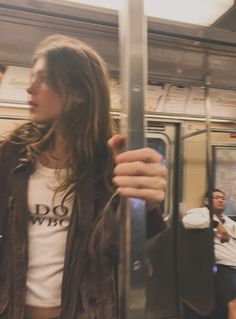 a woman with long hair standing on a subway train holding her hand up to the door