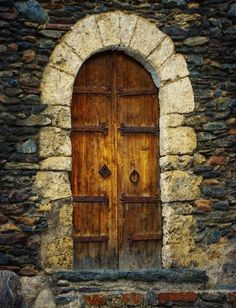 an old stone building with a wooden door and arched window in the center, surrounded by rocks