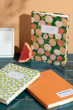 a grapefruit slice and two notebooks sitting on a tiled surface next to each other