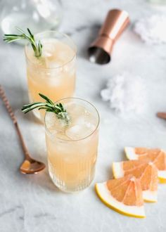 two glasses filled with lemonade and rosemary garnish next to sliced grapefruits