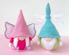 two crocheted gnomes are sitting next to each other on a pink surface