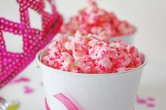 pink popcorn is in a white bucket on the table