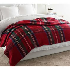 a red and black plaid blanket on top of a white bed with pillows in the background