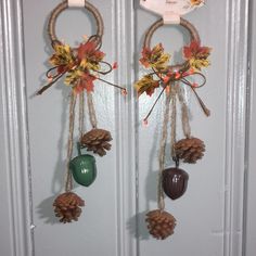 two pine cones and acorns hanging from hooks on a white door with autumn leaves