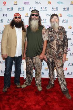 three men with long beards standing next to each other on a red carpeted area