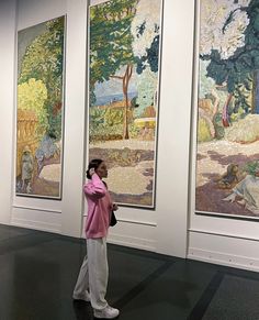 a woman standing in front of three paintings on display at an art gallery with one person taking a photo