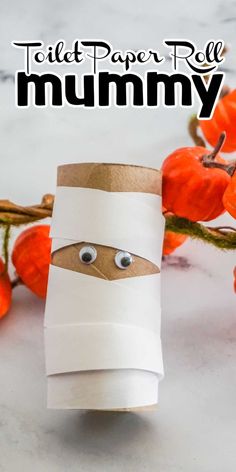 toilet paper roll mummy with eyes on it and some pumpkins in the background