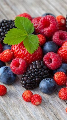 berries, raspberries, and blueberries are scattered on a wooden surface with a green leaf