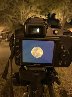 a camera with a full moon on the screen in front of some trees at night