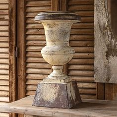 an old white vase sitting on top of a wooden table in front of a building