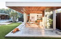 a dog laying on the grass in front of a house with an open patio area