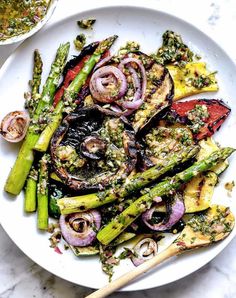 a white plate topped with asparagus and other veggies next to a bowl of sauce