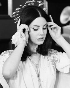 a woman wearing a tiara and holding her hands to her head while looking down