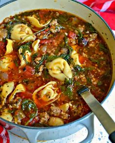 a pot filled with pasta and spinach soup on top of a red table cloth