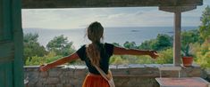 a woman in an orange skirt is standing on a porch with her arms spread out