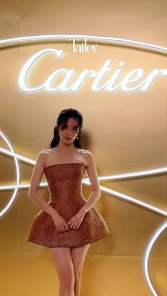 a woman standing in front of a sign wearing a short brown dress and high heels