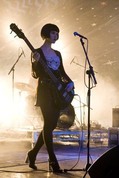 a woman standing in front of a microphone while holding a guitar