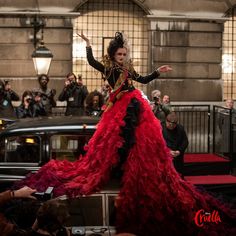 a woman in a red and black dress standing on top of a car with people around her