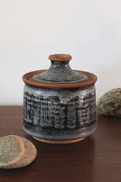 a ceramic jar sitting on top of a wooden table next to a rock and a stone