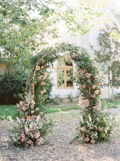 an outdoor wedding ceremony with flowers and greenery on the arch, in front of a white house