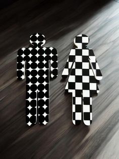 two black and white paper cut out figures sitting on top of a wooden floor next to each other