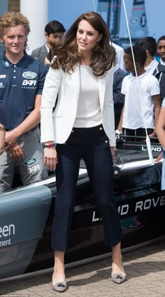 a woman in white jacket and black pants standing next to a boat with people watching