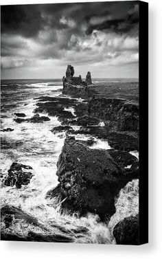 black and white photograph of waves crashing against rocks on the ocean shore with dark clouds overhead