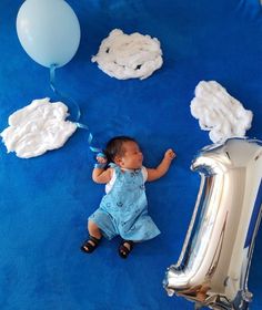 a baby laying on the ground next to balloons