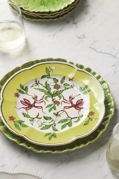 green and white plates with designs on them sitting on a marble counter top next to glasses