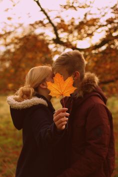 a man and woman kissing while holding an orange leaf in front of their face on a fall day