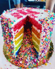 a rainbow cake with lots of sprinkles on the bottom and one slice cut out