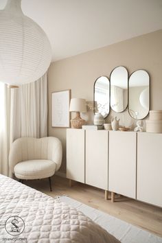 a bedroom with white furniture and mirrors on the wall, along with a round lamp