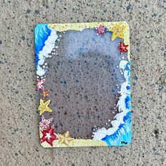 a square shaped mirror on the ground with starfishs and seashells painted on it