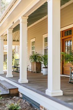 a porch with chairs and plants on the front steps, along with potted plants