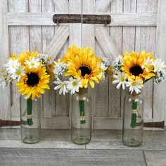 three glass vases with yellow and white flowers in front of a barn door,