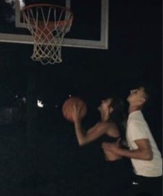 a man and woman playing basketball in the dark with a basket on his backboard