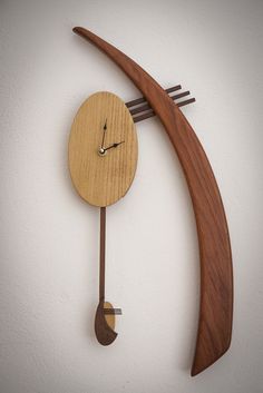 a wooden clock hanging from the side of a wall next to a curved piece of wood