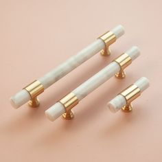 three white and gold knobs are on a pink surface, one is in the shape of a tube