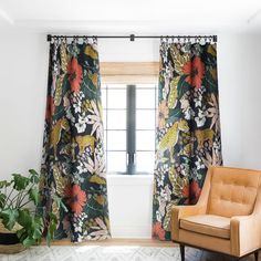 a living room with floral curtains and a chair in front of a window that has a potted plant next to it