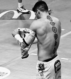 a shirtless man with tattoos on his back holding a wrestling glove in front of him