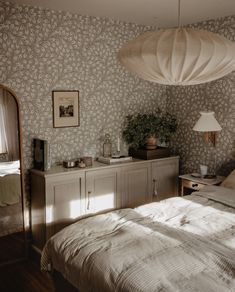 a bed room with a neatly made bed and a lamp hanging from the ceiling above it