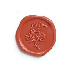 a red wax stamp with a flower design on the front and bottom, sitting on a white surface