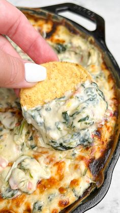 a hand dipping a tortilla chip into a skillet filled with spinach and cheese