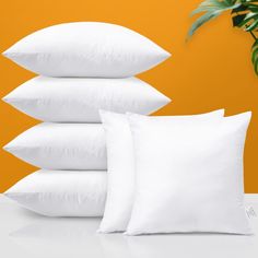 four pillows stacked on top of each other in front of an orange wall with a potted plant