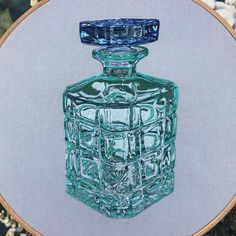 a green glass bottle sitting on top of a wooden table next to a cross stitch hoop