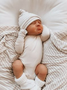 a baby is sleeping on a bed wearing a white hat and mittens, while wrapped in a blanket